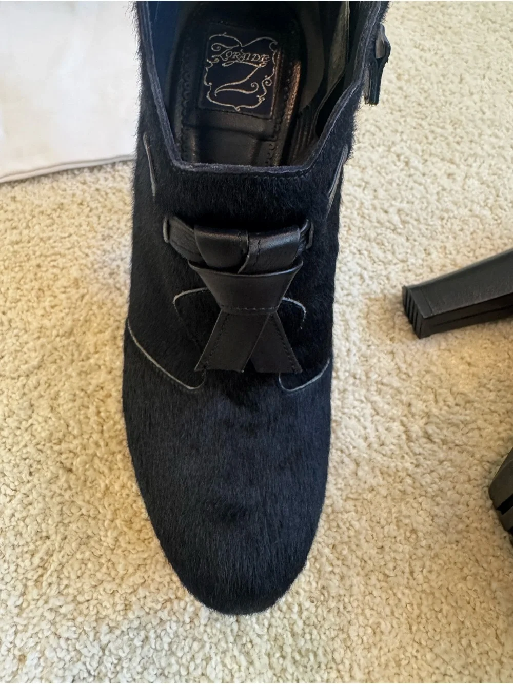 ZORAIDE black calf hair ankle booties with leather strap and tassel accents.